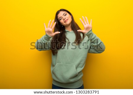Teenager girl with green sweatshirt on yellow background counting ten with fingers