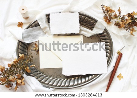 Styled stock photo. Winter, fall wedding, birthday table composition. Stationery mockup scene. Greeting cards, envelope, dry hydrangea flowers and calligraphy pen on silver tray. Flat lay, top view.