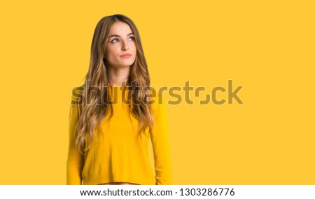 young girl with yellow sweater looking up with serious face on isolated yellow background