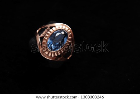 Jewelry on a fur background. Gold ring with a precious blue stone on a black background of natural fur trimmed otter.