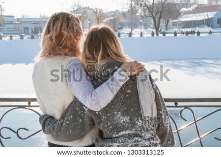 portrait of two embracing women mired in the snow by a frozen river in winter, rear view