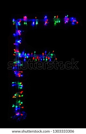 The letter "F" of the English alphabet made of multicolored electric garlands on a dark background, blur, bokeh, isolated on black