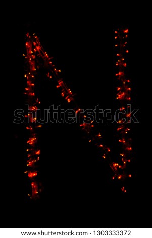 The letter "N" of the English alphabet made of red electric garland on a dark background, blur, bokeh, isolated on black