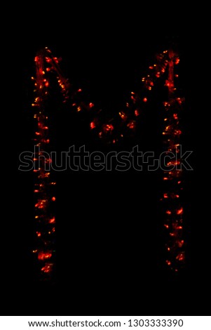 The letter "M" of the English alphabet made of red electric garland on a dark background, blur, bokeh, isolated on black