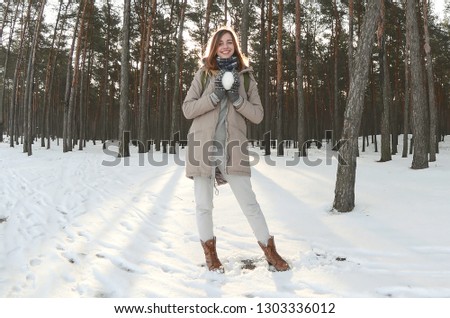 A young and joyful Caucasian girl in a brown coat holds a snowball in a snow-covered forest in winter. Fisheye Photo