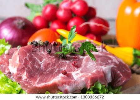Pork-neck meat steaks on lettuce on the background of radishes, tomato, red chili peppers, yellow chili peppers, green paprika, yellow paprika, red paprika, black pepper. Horizontal. Red onions,