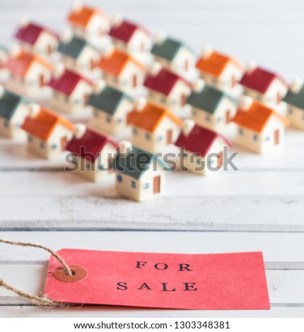 Red FOR SALE stamped text label tag with miniature houses on wooden white board. Conceptual image. Selective focus.