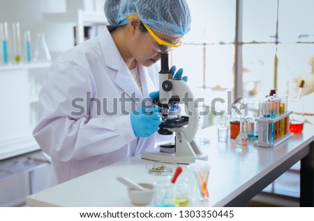 Picture of scientist asian woman using microscope with metal lens for research herb plant and medical equipment in laboratory
