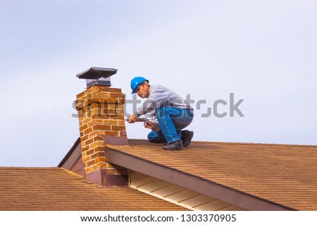 Contractor Builder with blue hardhat on the roof caulking chimney Royalty-Free Stock Photo #1303370905