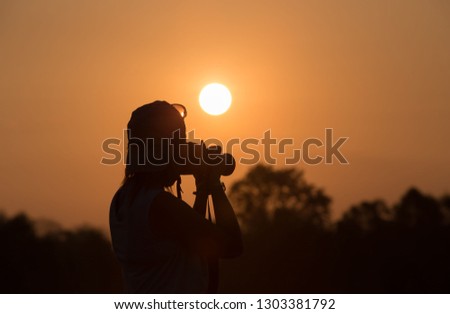 silhouette of a woman holding camera taking pictures outside during sunrise or sunset. Travelling and vacation concept / holiday traveling