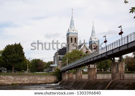 Small walking bridge over the Yamaska River to their grand, dual steepled church (Saint-Romuald), in Farnham, Quebec, on a very bright but slightly overcast day in late September.
