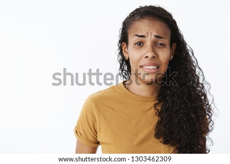 Yikes it bad. Portrait of worried awkward and displeased young clumsy african american female assistant frowning and clenching teeth as feeling guilty or unsure standing nervous over gray background Royalty-Free Stock Photo #1303462309