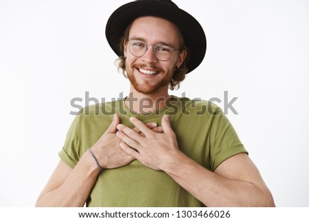 Oh thanks you should not have. Portrait of touched and delighted bday man with glasses, pierced nose and hat holding hands on body and smiling delighted, being thankful and happy receive present