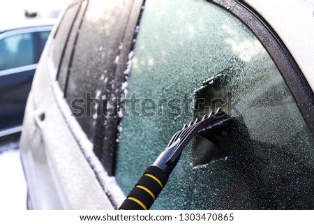 Cleaning an icy window on a car with ice scraper. Snow scraper. Cold snowy and frosty morning. Frozen car window