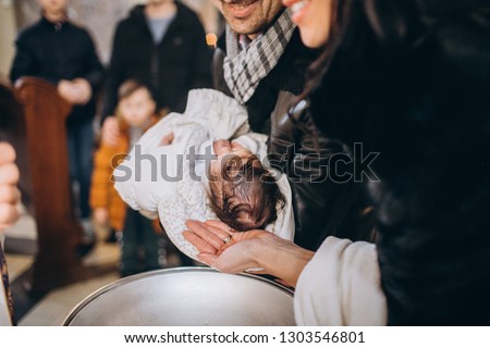 Baptism baby. Cute little head of a girl under holy water at christening ceremony with priest in church and bible