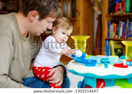 Happy proud young father having fun with baby daughter, family portrait together. Dad playing with baby girl with educational sorter toy with different colorful balls. Man with little child at home.