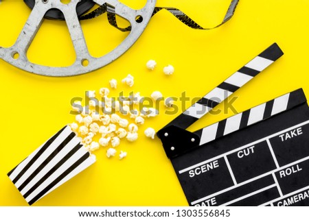 Movie premiere concept. Clapperboard, film stock, popcorn on yellow background top view