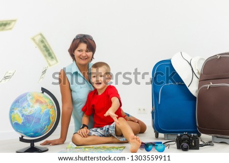 Family travel - young woman and boy sitting, lookin at a globe, while dollar banknotes fall