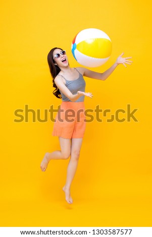 Happy young Asian woman in casual summer clothes playing beach ball in colorful yellow background