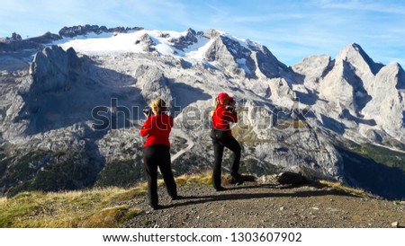 Two young women tourists taking picture of mountain landscape.  Marmolada Glacier. Dolomiti, Itay. Alps.