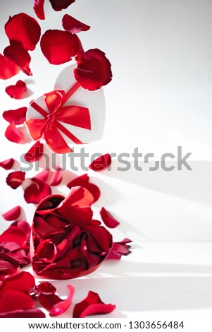 Heart shaped box with roses petals on white baclground. Flying rose petals