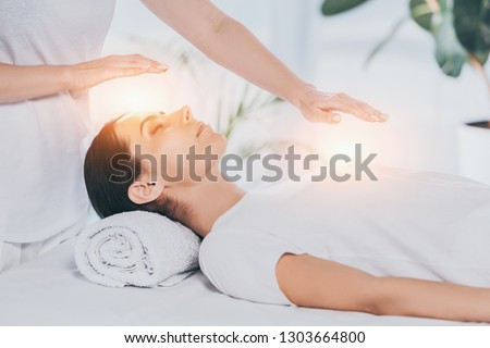 cropped shot of reiki healer doing therapy session to calm young woman with closed eyes Royalty-Free Stock Photo #1303664800