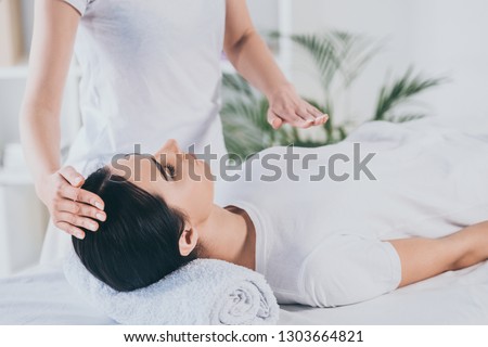 cropped shot of peaceful young woman receiving reiki healing treatment on head and chest Royalty-Free Stock Photo #1303664821
