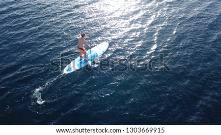 Aerial drone photo of fit man practising SUP or Stand Up Paddle surf board in deep blue meditteranean open sea