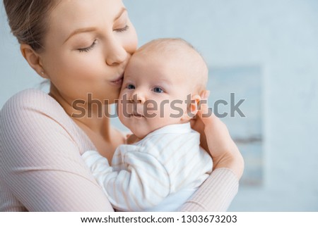 happy young mother kissing adorable infant baby at home