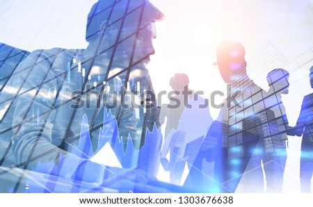 Bearded young businessman working with laptop with his colleagues silhouettes over cityscape background with double exposure of Forex graph. Toned image