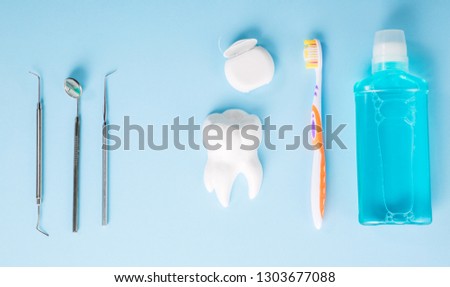 Dental health and teethcare concept. Professional steel dental instruments with a mirror near white tooth model, toothbrush, dental floss and mouthwash on light blue background.