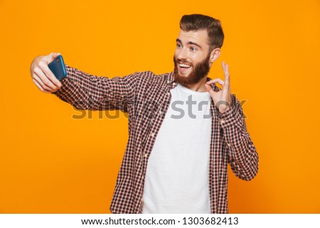 Portrait of a cheerful young man wearing casual clothes standing isolated over yellow background, taking a selfie