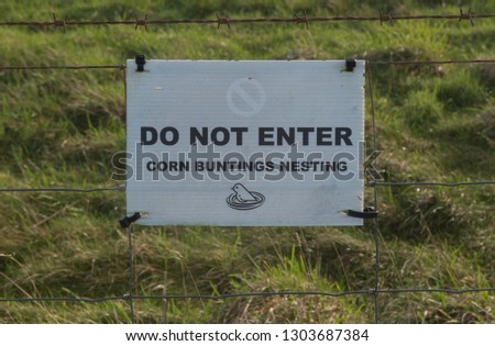 "Do Not Enter, Corn Buntings Nesting" Sign Attached to a Rusty Barbed Wire Fence by a Field on the South West Coast Path Between Porthcothan and Newquay in Rural Cornwall, England, UK