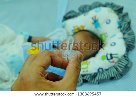 A picture of a naughty father want to give the pacifier to make his son quiet.
