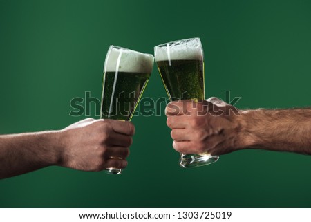 cropped view of men clinking  glasses of beer isolated on green, st patrick day concept