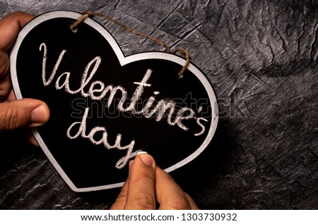 Closeup picture of hand writing Valentine´s day in heart shape a chalkboard over dark background