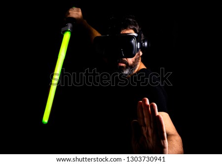 Bearded man playing virtual reality game using laser sword, black background