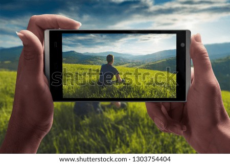 Man sitting on a hill in a green grass on a screen of smartphone taking by girl hand. Travel concept.