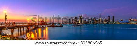 Panorama of Coronado old pier reflecting on in San Diego Bay from Coronado Island, California, USA. San Diego cityscape skyline with Downtown and Waterfront Marina District at twilight on background. Royalty-Free Stock Photo #1303806565
