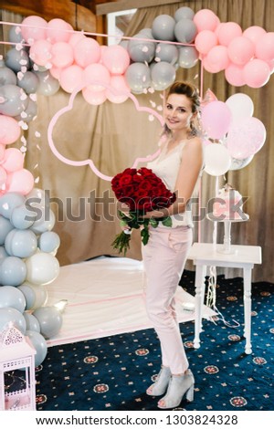 Portrait lady holding bouqet flowers on background grey and pink balloons. Beautiful happy young woman on birthday holiday party.