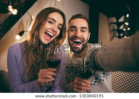 Beautiful happy young couple spending romantic evening together at home, drinking red wine, taking a selfie