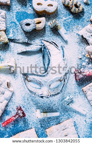 Carnival concept, elegant golden blue mask covered with lot sugar,circled by cookies and sweeties typical of carnival, like italian sfrappole or Chiacchiere, carnival fried pastry,flatly with lot o