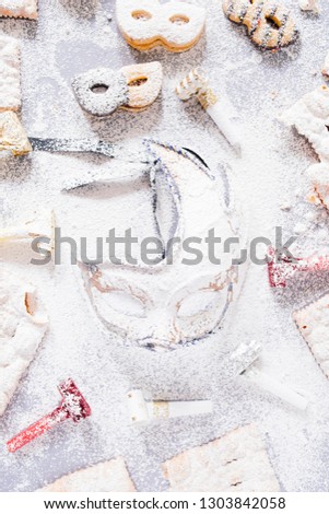 Carnival concept, elegant golden blue mask covered with lot sugar,circled by cookies and sweeties typical of carnival, like italian sfrappole or Chiacchiere, carnival fried pastry,flatly with lot o