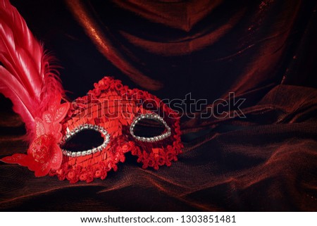 Photo of elegant and delicate red venetian mask over dark velvet and silk background