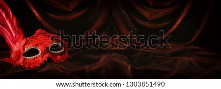 Photo of elegant and delicate red venetian mask over dark velvet and silk background