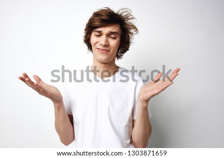 Cute guy in a white T-shirt disheveled hair to keep his hands in front of him on a gray background