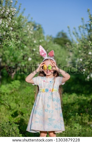 Cute girl with bunny ears on Easter day. A girl is chasing Easter eggs in the garden. The girl has a basket with painted eggs.