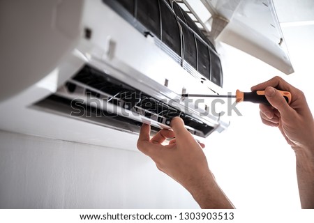Electrician repairing air conditioner indoors Royalty-Free Stock Photo #1303903513