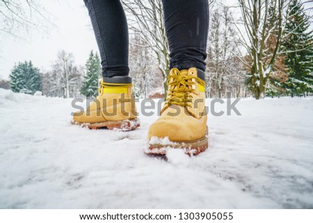 Winter Walk in Yellow Leather Boots. Front view on the feet of a man walking along the icy snowy pavement. Pair of shoe on icy road in winter. Abstract empty blank winter weather background