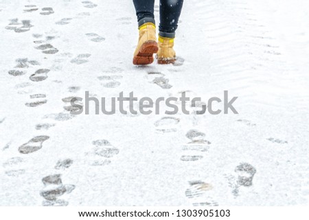 Winter Walk in Yellow Leather Boots. Back view on the feet of a man walking along the icy snowy pavement. Pair of shoe on icy road in winter. Abstract empty blank winter weather background